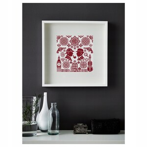 May include: A framed cross-stitch artwork featuring red silhouettes of Sherlock Holmes and Dr. Watson, along with iconic symbols like a pistol, violin, and Big Ben. The artwork is displayed in a white square frame.