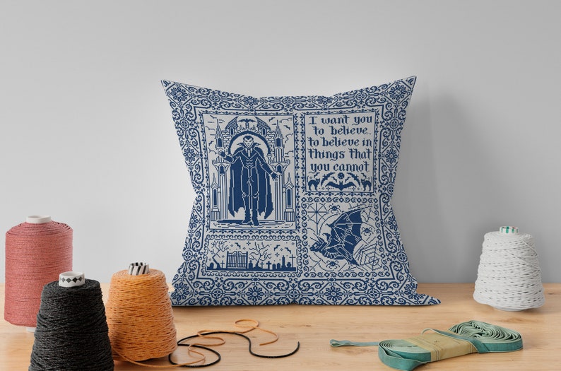 Puede incluir: Una almohada azul y blanca con un dise&ntilde;o g&oacute;tico que presenta un vampiro, murci&eacute;lagos y el texto "Quiero que creas... creer en cosas que no puedes".