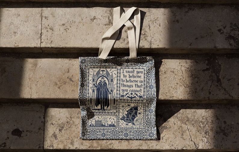 Puede incluir: Una bolsa de tela beige con un dise&ntilde;o estampado en azul y blanco. La bolsa presenta una ilustraci&oacute;n de estilo g&oacute;tico de un hombre con una capa y una cita que dice "Quiero que creas, que creas en cosas que no puedes."
