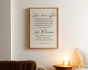 May include: A framed print with a white background and black text. The text reads "Liebe deinen Gott" and "Liebe Mitmenschen". The text is in a cursive font. The print is hanging on a white wall.