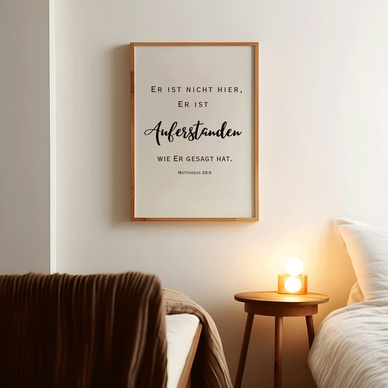 May include: A framed print with a white background and black text that reads "ER IST NICHT HIER, ER IST AUFERSTANDEN WIE ER GESAGT HAT. MATTHAEUS 28:6". The print is hanging on a white wall.
