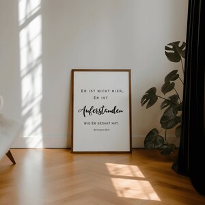 May include: A framed print with a white background and black text that reads "ER IST NICHT HIER, ER IST AUFERSTANDEN WIE ER GESAGT HAT. MATTHAEUS 28:6".