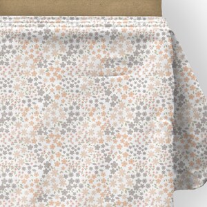 May include: A bolt of white fabric featuring a repeating pattern of small, delicate flowers in shades of soft peach and muted grey. The floral print is densely arranged across the surface, with tiny green leaves interspersed among the blossoms.