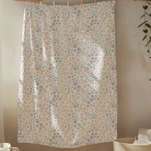 May include: A rectangular fabric panel featuring a dense, repeating floral pattern in soft shades of muted peach and light gray against a white background. The textile is suspended from a horizontal line by small wooden clips at the top edge.