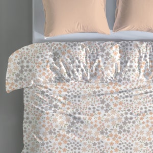 May include: A white duvet cover featuring a repeating floral pattern in shades of peach, light gray, and muted green. The bedding is paired with two solid peach-colored pillows positioned at the top of the bed, creating a coordinated bedroom set.