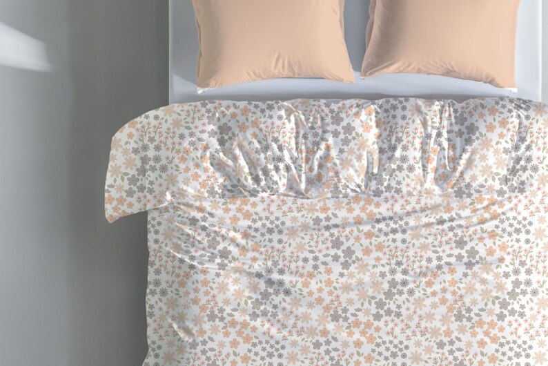 May include: A white duvet cover featuring a repeating floral pattern in shades of peach, light gray, and muted green. The bedding is paired with two solid peach-colored pillows positioned at the top of the bed, creating a coordinated bedroom set.