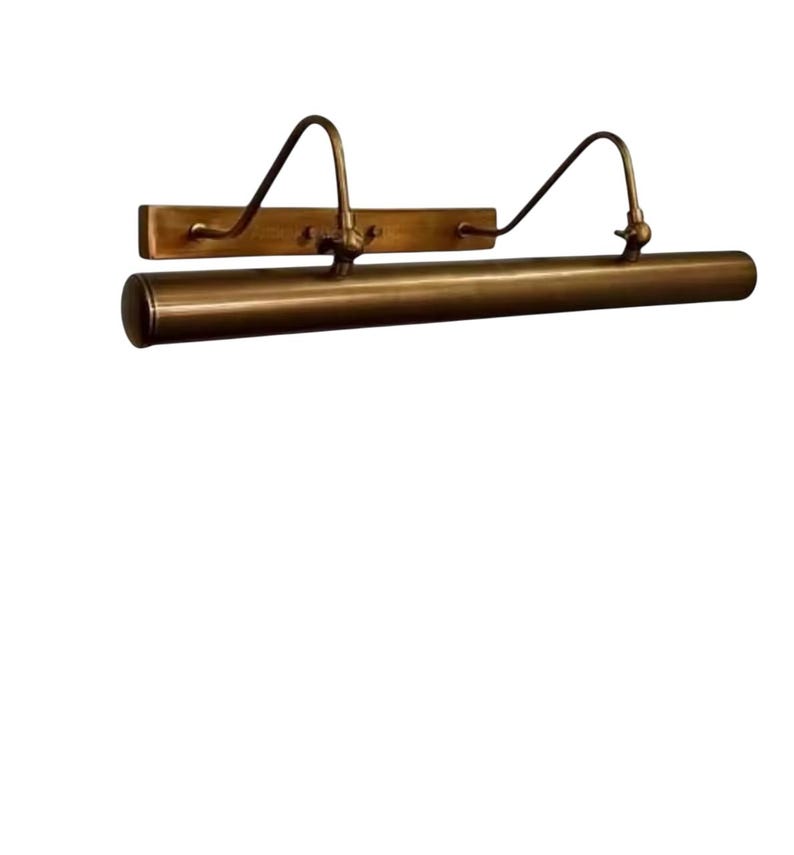 May include: A brass picture light, featuring a rectangular backplate and a cylindrical light housing. Two curved arms connect the backplate to the light. This vintage-style light fixture is designed to illuminate artwork, with a warm, inviting glow.