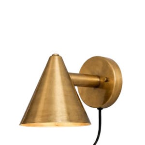 May include: A wall-mounted lamp featuring a conical brass shade and a circular brass backplate. The fixture includes a horizontal arm connecting the shade to the base and a black power cord extending from the bottom of the circular wall mount.