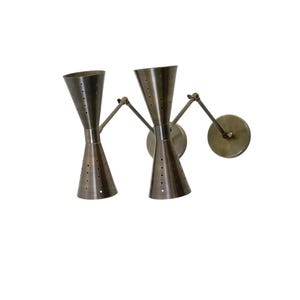 May include: A pair of vintage-style wall sconces. Each sconce features a conical shade with small perforations, a central cylindrical section, and an adjustable arm. The sconces are made of a metallic material with a bronze finish.