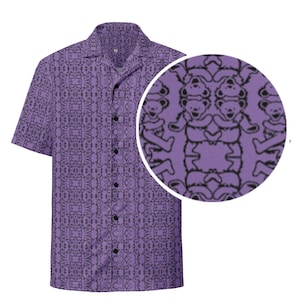 May include: A short-sleeved button-down shirt in a lavender hue, featuring a repeating pattern of black bear figures. The shirt has a classic collar and a button-up front. A circular inset shows a close-up of the bear pattern.