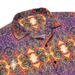 May include: A purple and orange button-up shirt with a psychedelic pattern. The pattern features a repeating design of skulls and lightning bolts.