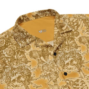 May include: A yellow button-up shirt with a floral and skull print. The shirt has a collar and a button closure. The inside of the collar is a solid yellow color.