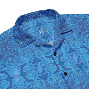 May include: A blue button-up shirt with a repeating pattern of a lightning bolt inside a blue and white swirl. The shirt has a collar and a button closure.