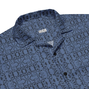 May include: A blue short-sleeved button-down shirt featuring a repeating black line-art pattern of dancing bears. The shirt has a classic collar and a white interior neck label with the text "Tattooed Artworks" printed in black ink.