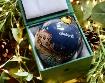May include: A blue glass Christmas ornament with a painted scene of Edinburgh, Scotland. The ornament is in a green velvet box with a white satin lining. The ornament has gold accents and the text "Edinburgh" is written on the front.