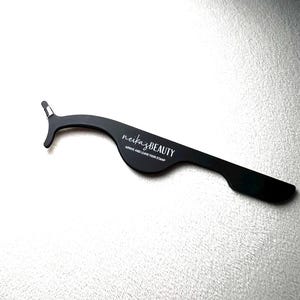 Könnte beinhalten: Schwarzes Wimpernapplikator-Werkzeug mit dem Text "neika BEAUTY" und "ARRIVE AND LEAVE YOUR STAMP" darauf gedruckt.