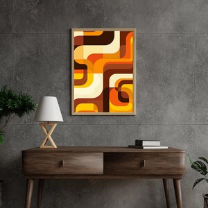 Puede incluir: Una impresión abstracta enmarcada con formas geométricas en tonos marrones, naranjas y amarillos. La impresión está colgada en una pared gris sobre una mesa consola de madera.