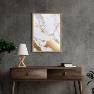 Puede incluir: Una impresión enmarcada de un fondo de mármol blanco con vetas doradas. La impresión está colgada en una pared gris sobre una mesa consola de madera con dos cajones.
