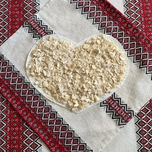 Puede incluir: Un montón de masa blanca seca y desmenuzada en forma de corazón sobre un mantel blanco con un patrón bordado rojo y negro.