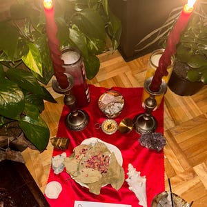 K&ouml;nnte beinhalten: Ein roter Samtaltartuch mit zwei brennenden roten Kerzen, einem Kompass, Kristallen und einer Schale mit Lorbeerbl&auml;ttern und Rosenbl&uuml;ten. Ein handgeschriebener Zettel lautet "Bimpe's Magical Shop ♡♡".