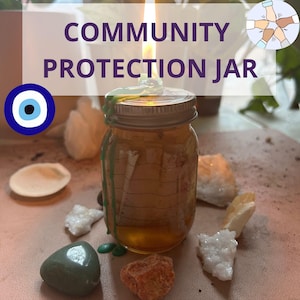 May include: A glass jar with a gold lid and a lit candle inside. The jar is filled with a golden liquid and has green wax drippings on the outside. The jar is surrounded by various stones, including a green stone, a red stone, and a white stone. The jar is labeled "COMMUNITY PROTECTION JAR".