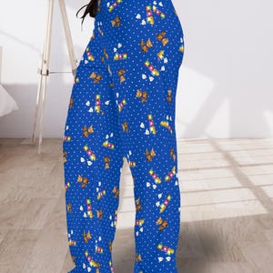 May include: Blue pajama trousers featuring a white polka dot pattern and a repeating design of teddy bears and building blocks. The trousers have a drawstring waist and a relaxed fit.
