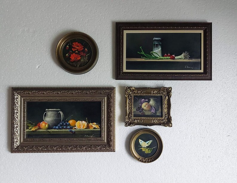 K&ouml;nnte beinhalten: Eine Sammlung gerahmter Stillleben-Gem&auml;lde. Die Kunstwerke zeigen verschiedene Motive, darunter Blumen, Fr&uuml;chte und Gem&uuml;se. Die Rahmen sind verziert und in Braun- und Goldt&ouml;nen gehalten. Die Gem&auml;lde h&auml;ngen an einer wei&szlig;en Wand.