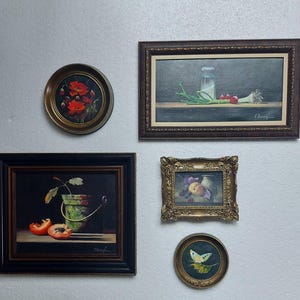 K&ouml;nnte beinhalten: Eine Sammlung gerahmter Vintage-&Ouml;lgem&auml;lde, die an einer wei&szlig;en Wand ausgestellt sind. Die Gem&auml;lde zeigen verschiedene Stillleben, darunter Blumen, Fr&uuml;chte und Gem&uuml;se. Die Rahmen variieren im Stil, von verziertem Gold bis zu einfachem dunklem Holz.