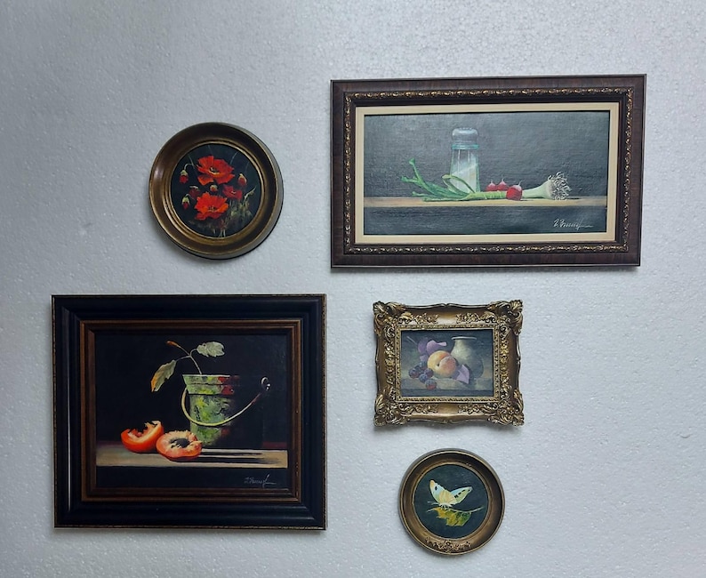 K&ouml;nnte beinhalten: Eine Sammlung gerahmter Vintage-&Ouml;lgem&auml;lde, die an einer wei&szlig;en Wand ausgestellt sind. Die Gem&auml;lde zeigen verschiedene Stillleben, darunter Blumen, Fr&uuml;chte und Gem&uuml;se. Die Rahmen variieren im Stil, von verziertem Gold bis zu einfachem dunklem Holz.