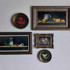 Puede incluir: Una composici&oacute;n de pared de galer&iacute;a con cinco pinturas al &oacute;leo enmarcadas. La colecci&oacute;n incluye una pintura redonda de amapolas rojas, un bodeg&oacute;n rectangular de frutas y una jarra, una pintura rectangular de r&aacute;banos, un peque&ntilde;o bodeg&oacute;n de frutas ornamentado y una pintura redonda de una mariposa amarilla.