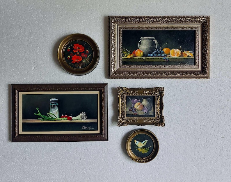Puede incluir: Una composici&oacute;n de pared de galer&iacute;a con cinco pinturas al &oacute;leo enmarcadas. La colecci&oacute;n incluye una pintura redonda de amapolas rojas, un bodeg&oacute;n rectangular de frutas y una jarra, una pintura rectangular de r&aacute;banos, un peque&ntilde;o bodeg&oacute;n de frutas ornamentado y una pintura redonda de una mariposa amarilla.