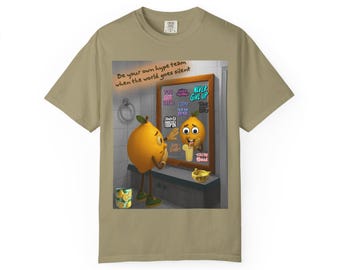 May include: A tan t-shirt featuring a cartoon lemon looking in a mirror. The mirror shows a smiling lemon with motivational phrases. The text "Be your own hype team when the world goes silent" is above the mirror.