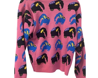 Könnte beinhalten: Rosa Strickpullover mit einem sich wiederholenden Muster aus pixeligen Elefanten in Schwarz, Blau und Gelb. Der Pullover hat einen Rundhalsausschnitt und lange Ärmel. Die Elefanten sind in einem gitterartigen Muster angeordnet.