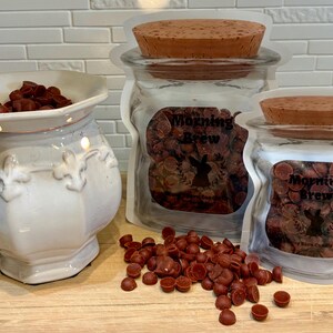 Op de afbeelding: Een witte keramische waxwarmer met een decoratief ontwerp, gevuld met donkerbruine waxmelts. Twee doorzichtige zakken met kurken deksels en de tekst "Morning Brew" zijn gevuld met vergelijkbare waxmelts.