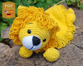 May include: A crocheted lion toy with a yellow mane and a white face. The lion is lying on a wooden surface.
