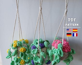May include: Three handmade crochet hanging planters with trailing vines and flowers in yellow, purple, and pink. The planters are suspended by white cords from a wooden shelf. The text "PDF PATTERN" is visible in the image.