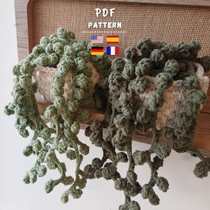 May include: Two crocheted hanging plants with trailing vines in shades of green and olive green. The plants are in rectangular, off-white crocheted pots. The text "PDF PATTERN" is above the plants.