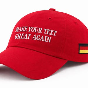 Puede incluir: Gorra de béisbol roja con la frase "MAKE YOUR TEXT GREAT AGAIN" bordada en blanco. Un pequeño parche con la bandera alemana está en el lateral. La gorra tiene una visera curva.