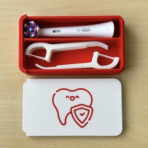 May include: A red rectangular container holding a white electric toothbrush, two white floss picks, and a toothbrush head with purple and blue bristles. A white card with a red tooth graphic and shield is below.