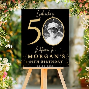 May include: Black and gold birthday sign with the number 50 and the text "Look who's 50. Welcome to Morgan's 50th Birthday 02.12.2025". A black and white photo of a young boy is in the center of the sign.