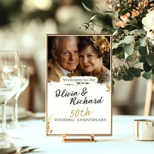 Puede incluir: Un letrero de mesa dorado con una foto de una pareja mayor, el texto "Bienvenido a Olivia & Richard 50 aniversario de boda" y detalles en pan de oro.