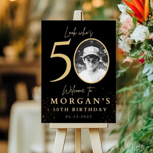 May include: Black and gold welcome sign with a photo of a young boy wearing a baseball cap. The sign says "Look who's 50, Welcome to Morgan's 50th Birthday, 02.12.2025".