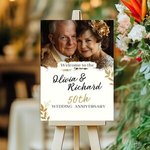 Puede incluir: Bienvenido al cartel del 50 aniversario de boda de Olivia y Richard con una foto de una pareja mayor. El cartel es blanco con letras doradas y un dise&ntilde;o de hojas doradas.