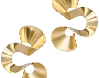 May include: A pair of gold-toned earrings featuring a continuous, fluid ribbon-like design that forms two open, circular loops. The metal surface has a smooth, polished finish with gentle curves that create a sense of movement and depth.