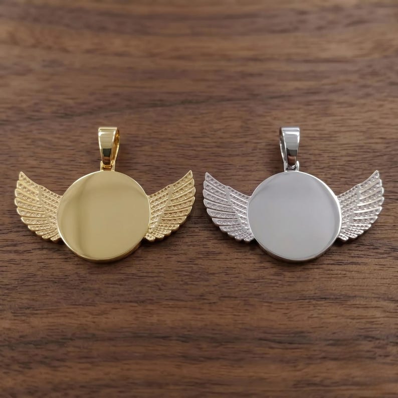 May include: Two circular pendants with attached wings on each side. One pendant is polished gold-tone metal, and the other is polished silver-tone metal. Each piece features a smooth, round center and a small bail at the top for hanging.