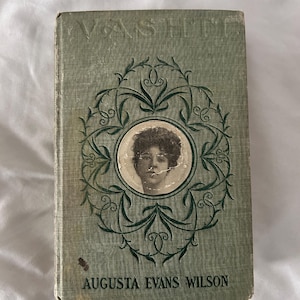 May include: Vintage book titled "Vashti" by Augusta Evans Wilson. The cover is a faded green with a decorative green floral design around a portrait of a woman. The book shows signs of wear.
