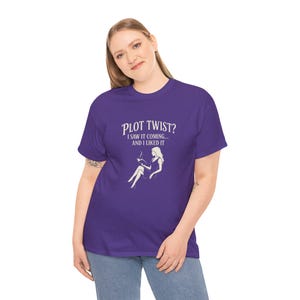 May include: Purple t-shirt with a white graphic that says "Plot Twist? I saw it coming... and I liked it." The graphic also features a white silhouette of a woman sitting with a book and a cup of coffee.