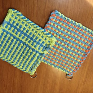 May include: Two woven pot holders with green, blue, and orange stripes. Each pot holder has a metal ring attached.
