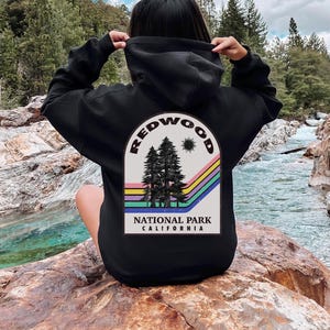 May include: Black hooded sweatshirt with a vintage-style graphic of Redwood National Park, California. The graphic features a rainbow arch, three trees, and the text "REDWOOD NATIONAL PARK CALIFORNIA".