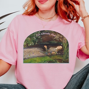 May include: A light pink short-sleeve t-shirt featuring a graphic print of the painting Ophelia by John Everett Millais inside an arched frame. The text "I'm Literally Fine" is printed in a white serif font above the painting.